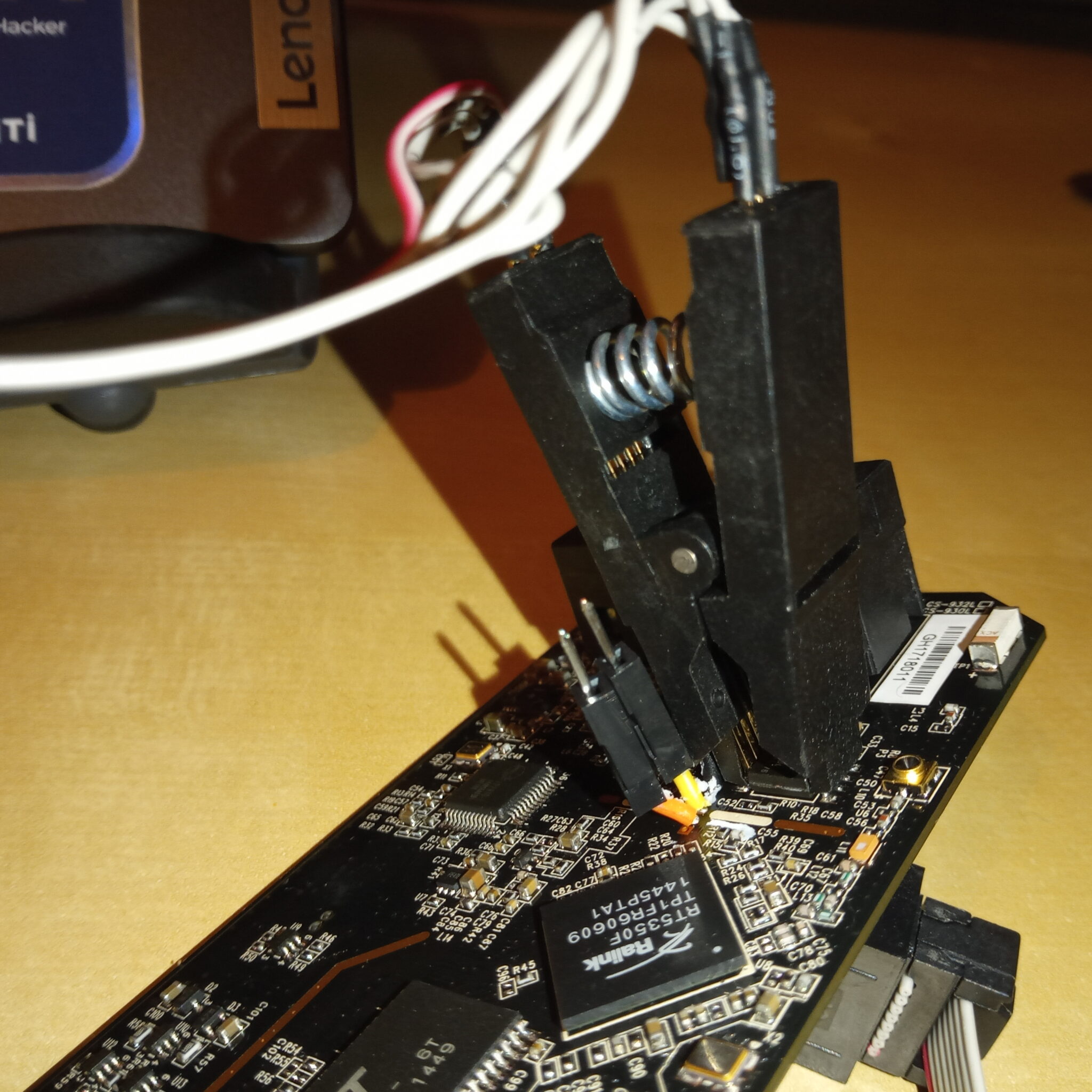 基板のうえから大きなクリップでフラッシュメモリと思われるチップを挟んでいる様子。クリップはPCにつながっている